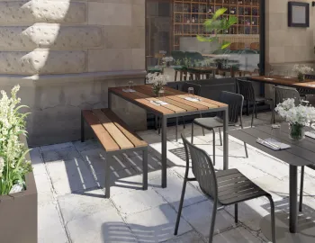Cape Dining Table with a brown slatted top and charcoal frame beside a matching bench on a restaurant terrace