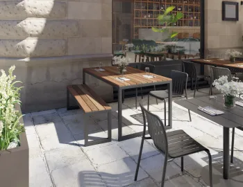 Lilico Dining Table with brown slats and charcoal box end legs beside a matching bench on a restaurant terrace