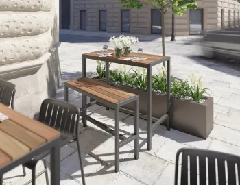 Moonah High Bar Table and bench with brown slats and charcoal frames beside planters on a restaurant terrace