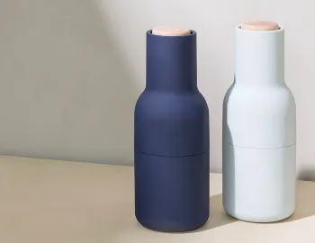 Navy and pale blue Audo Bottle Grinders with wooden lids standing together on a pale surface
