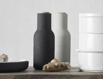 Charcoal and light grey Audo Bottle Grinders with pale wooden lids beside ginger and a white canister