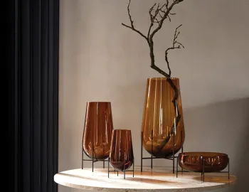 Three amber Échasse Vases and a matching bowl on dark stands, with a branch in the tallest vase