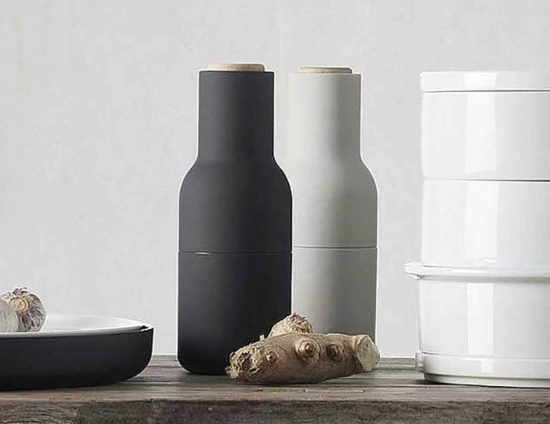 Charcoal and light grey Audo Bottle Grinders with pale wooden lids beside ginger and a white canister