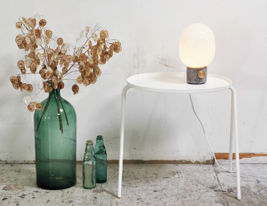 JWDA Concrete Table Lamp on a white tray table beside green bottles holding dried branches