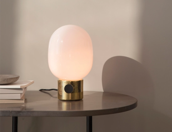 Brass JWDA Table Lamp glowing beside stacked books on a round dark table