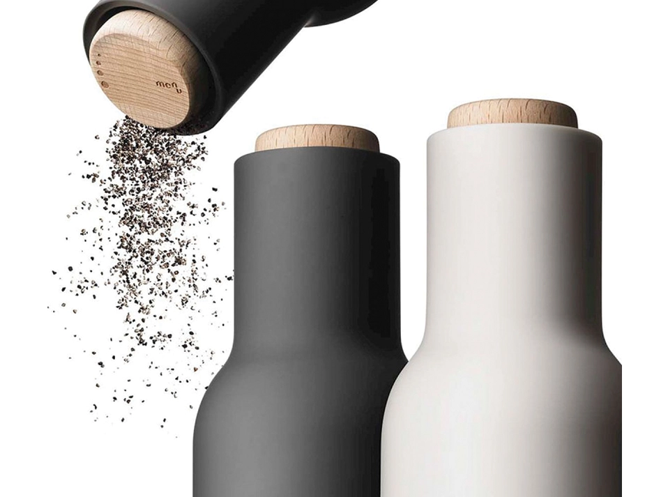 Audo Bottle Grinder dispensing ground pepper from its wooden top beside charcoal and light grey grinders