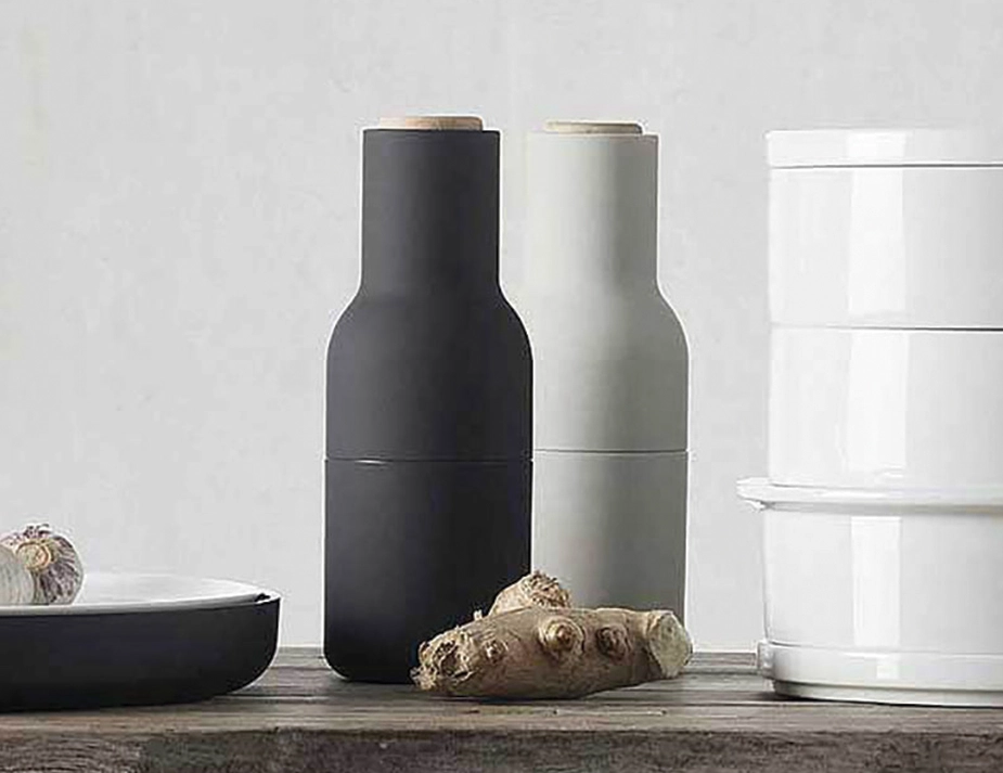 Charcoal and light grey Audo Bottle Grinders with pale wooden lids beside ginger and a white canister