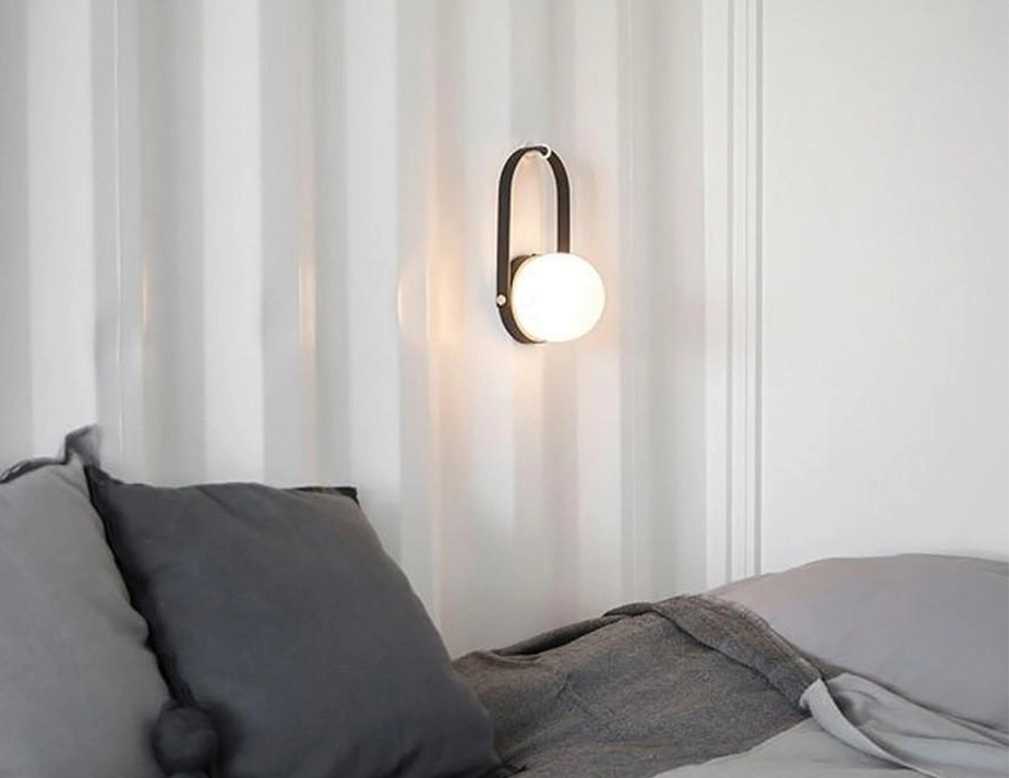 Glowing black Carrie Table Lamp hanging from a wall hook above grey pillows and bedding