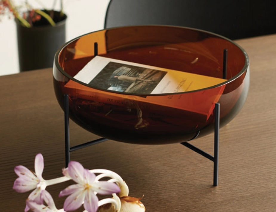 Amber Échasse Bowl holding a book on a wooden table, with its dark supporting stand visible