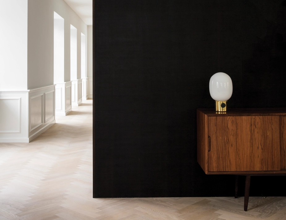 Brass JWDA Table Lamp on a wooden sideboard against a black wall beside a bright corridor