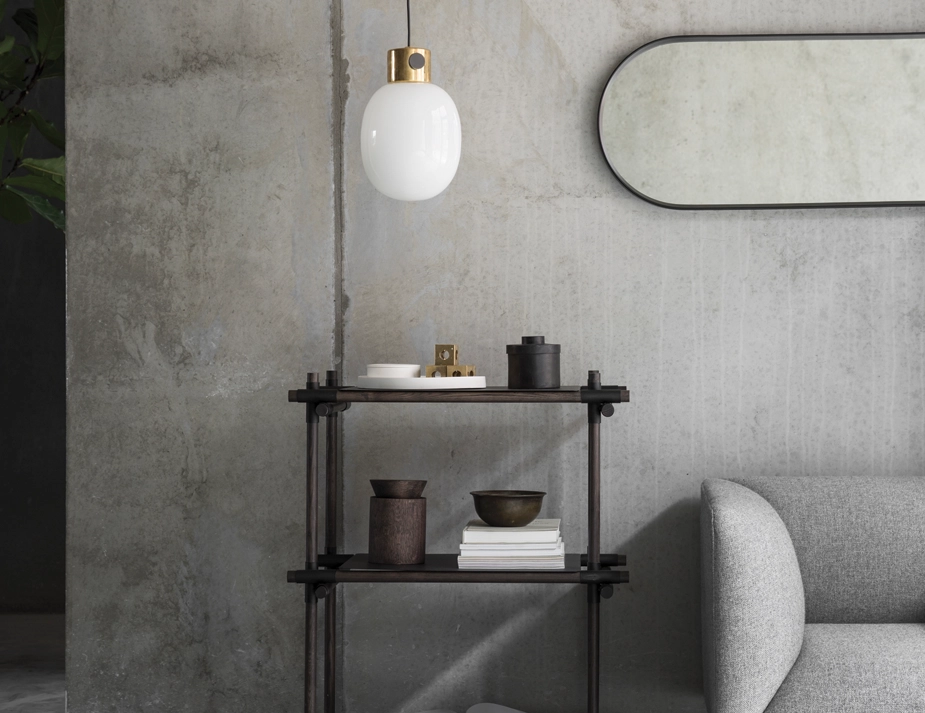 Black oval Norm Wall Mirror hung horizontally above a dark shelving unit beside a grey sofa